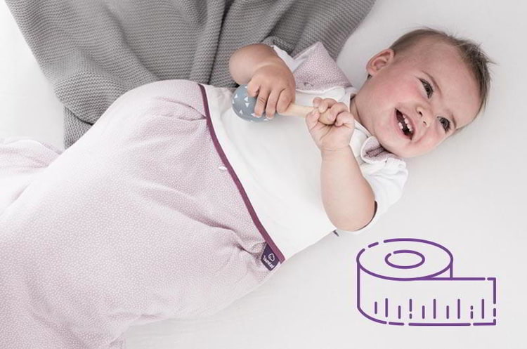 Baby im rosa Träumeland Schlafsack im Bett mit Illustration von einem Maßband Baby im rosa Träumeland Schlafsack im Bett mit Illustration von einem Maßband