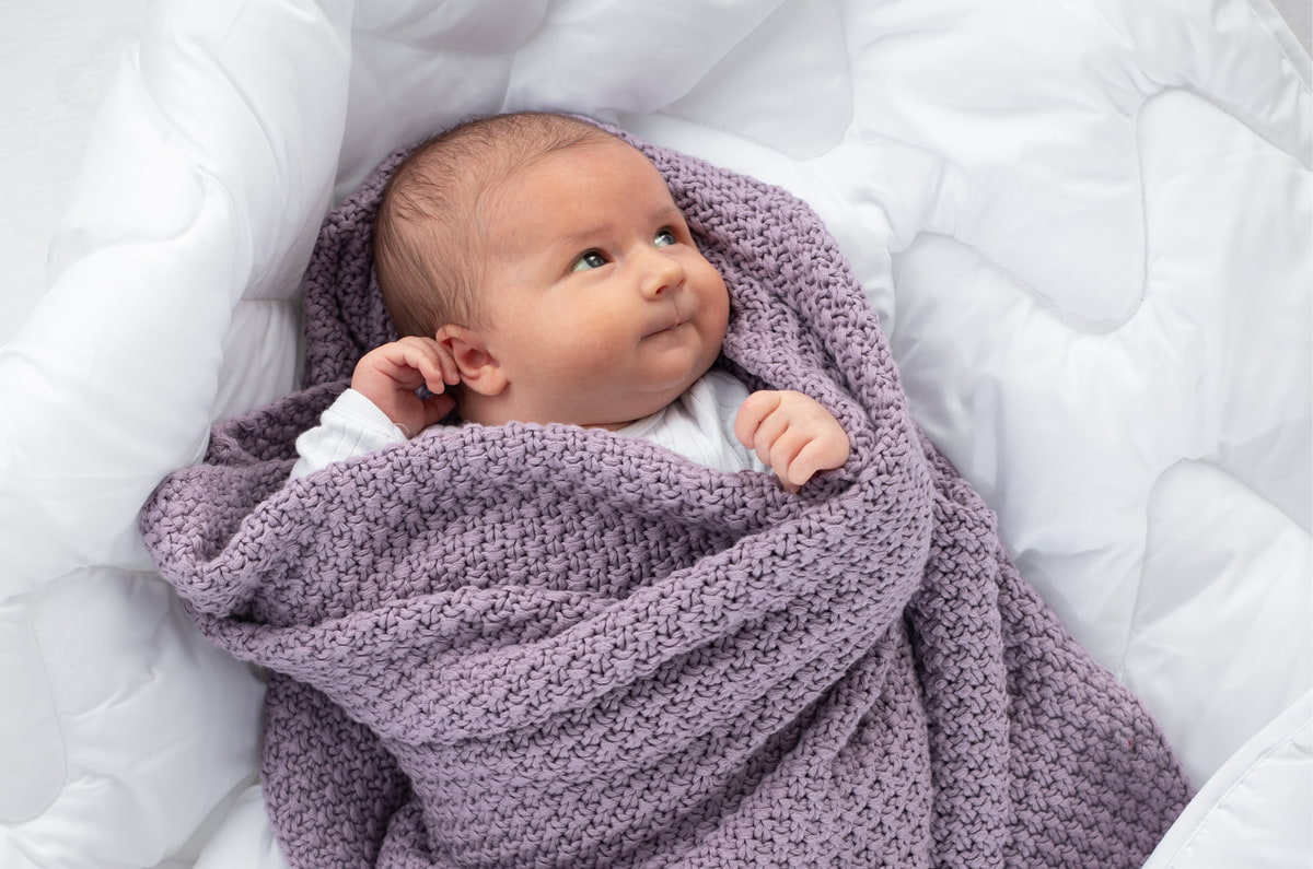 Baby eingewickelt in gestrickte lila Decke Baby eingewickelt in gestrickte lila Decke