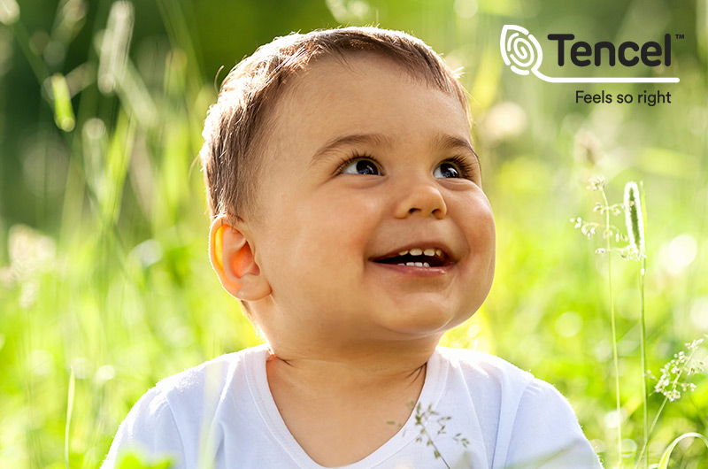Baby im Gras sitzend mit TENCEL-Logo Baby im Gras sitzend mit TENCEL-Logo