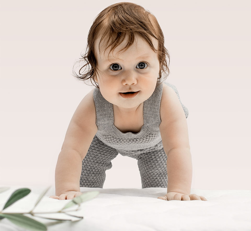 Baby im grauen Strampler mit beigem Hintergrund
