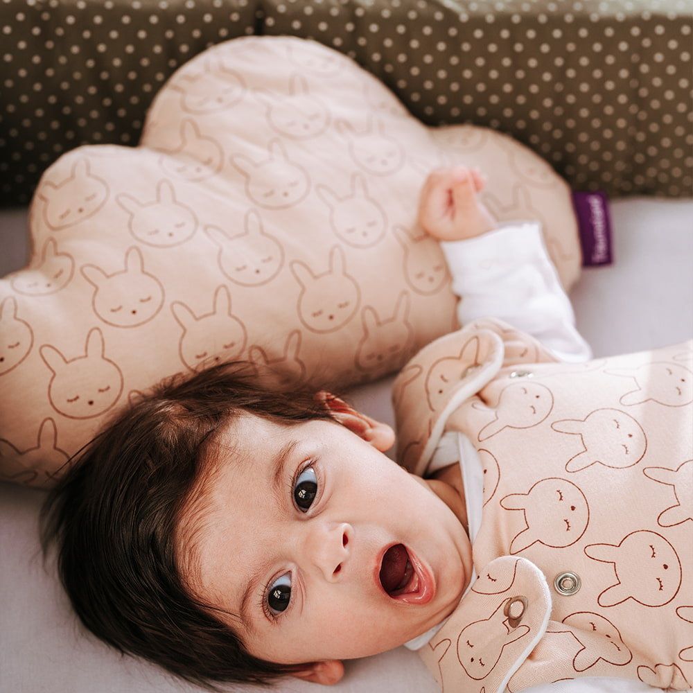Baby gähnend im Babybett mit Kuschelkissen