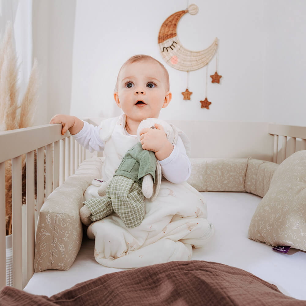 Baby sitzend im Gitterbett mit Schlafsack